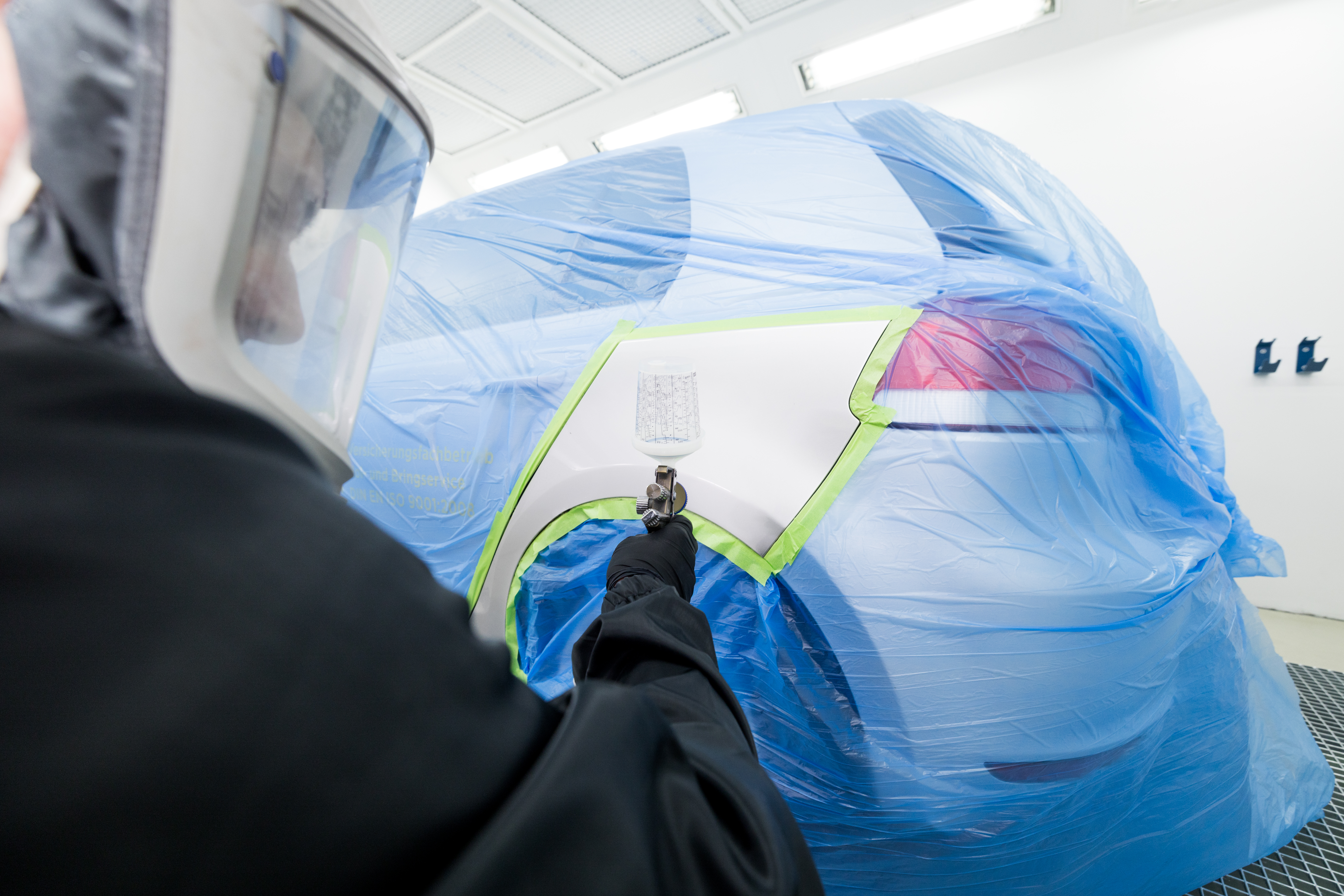 Lackierer in voller Ausrüstung in der Seitenansicht beim Lackieren eines Fahrzeuges