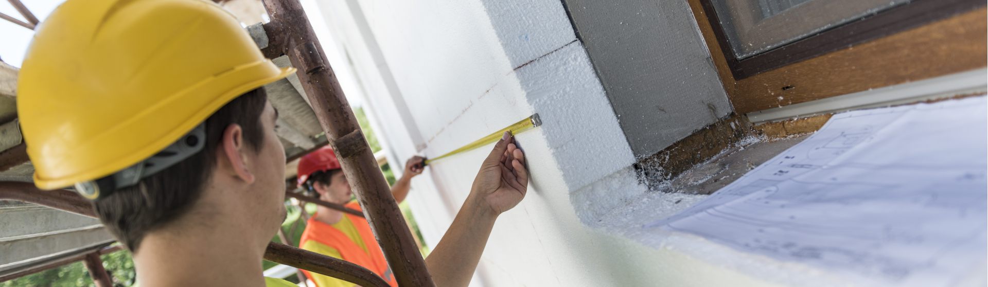 Praktikanten mit Schutzweste und Schutzhelm auf der Baustelle hält ein Maßband und nimmt Maß